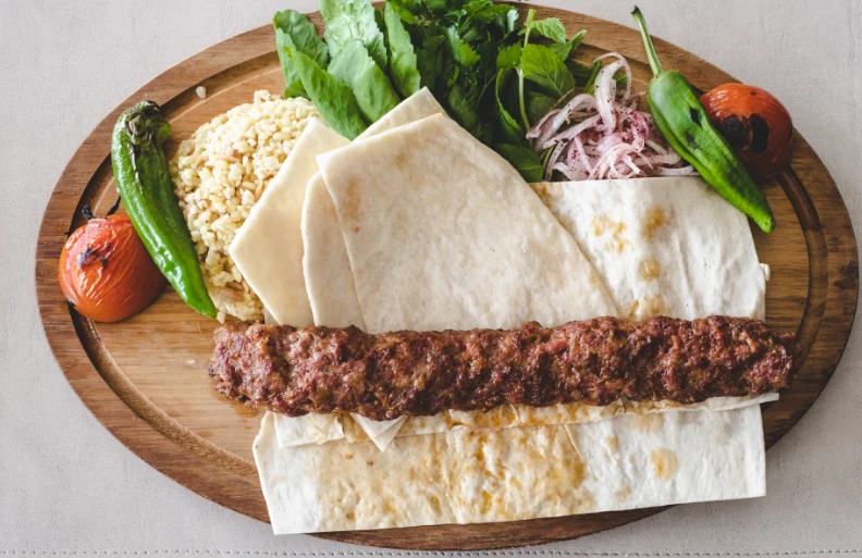 Charred Adana kebab on wide metal skewers over a charcoal grill