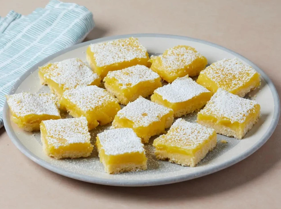 Üstü hafif pudra şekerli, sarı limon dolgulu ve açık altın renkli kıtır tabanlı kare limonlu bar dilimleri