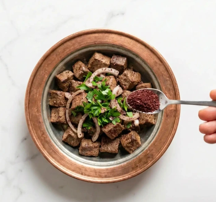 Sumaklı kırmızı soğan ve küp patates yanında servis edilen kızarmış Arnavut ciğeri