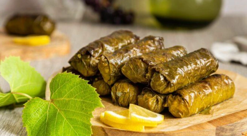 Limon dilimleriyle servis edilen ince sarılmış zeytinyağlı asma yaprak sarmaları
